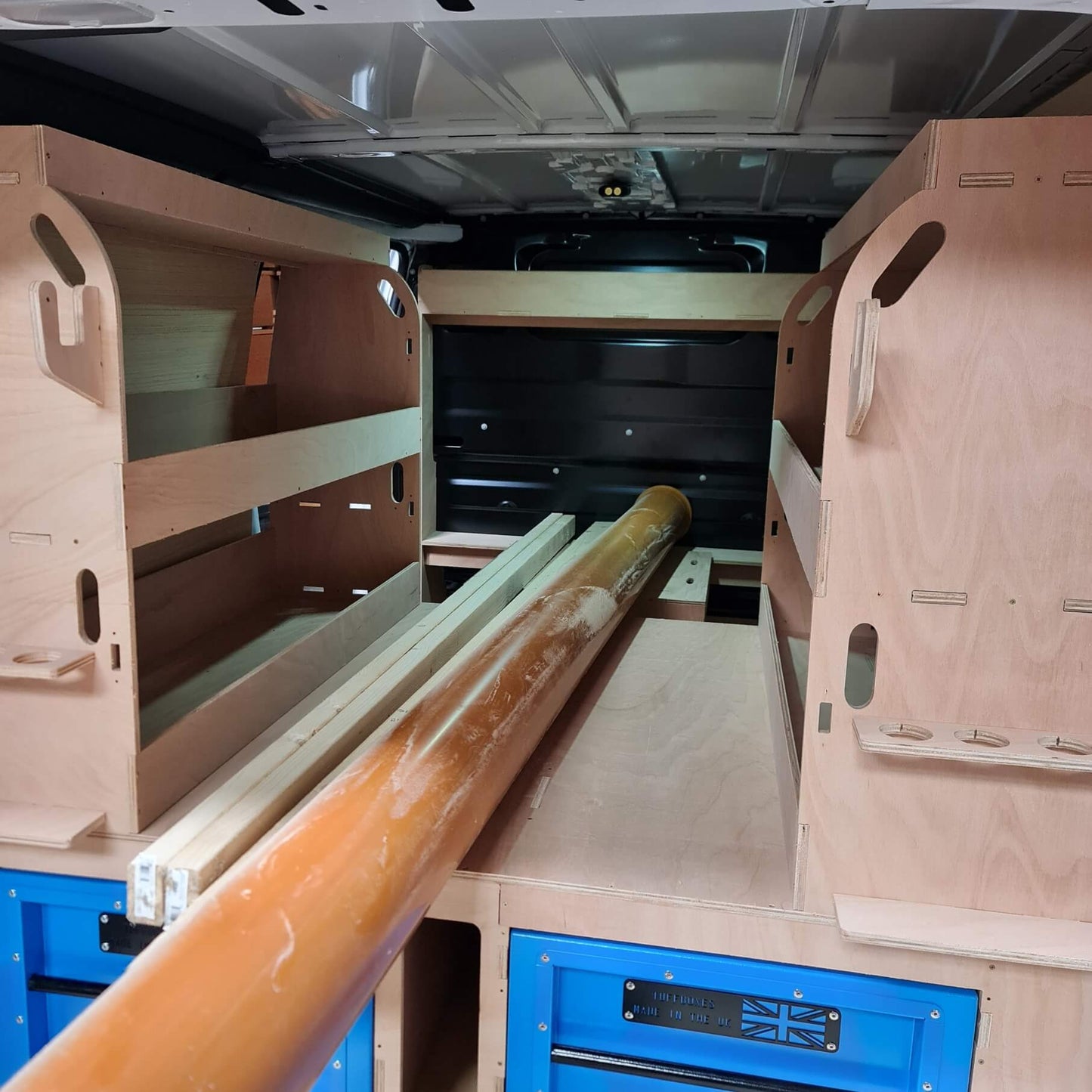 Wooden bunk beds with a long wooden beam inside a vehicle.