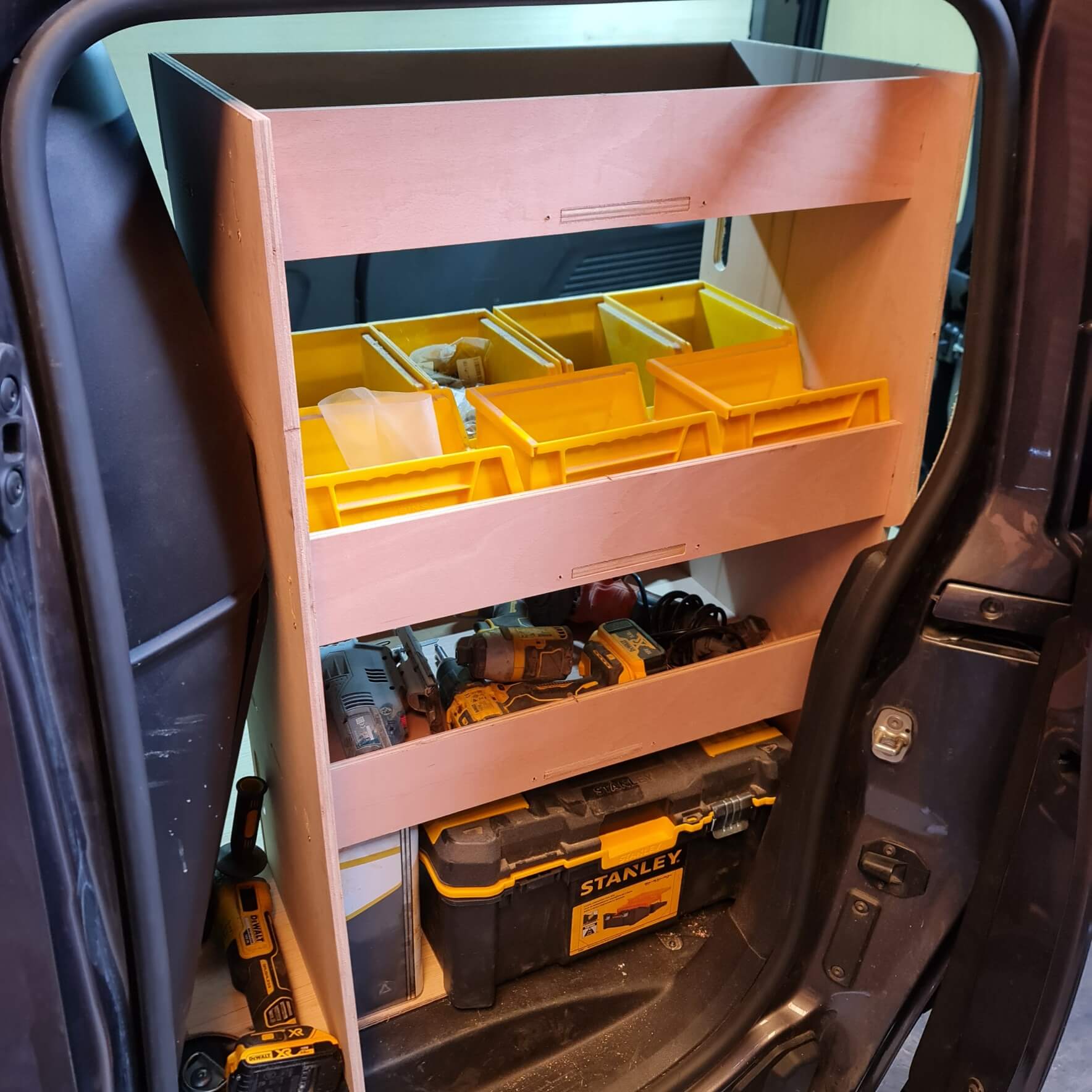Tool storage cart with yellow trays and tools inside a vehicle.