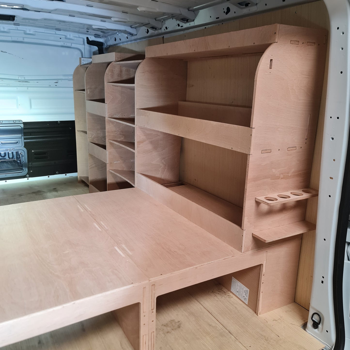 A set of plywood raised floors and racking system installed inside the cargo area of a Peugeot Expert LWB van, featuring various shelves and storage compartments.