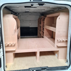 Interior view of a van's cargo area showing a wooden raised floor and storage shelves, with an open door and a viewing window.