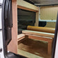 Van interior with wooden bed setup and folded seats.
