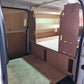 Van interior with wooden panels and floor, showing a DIY conversion process.
