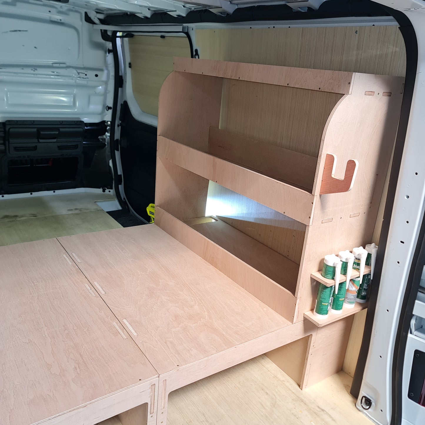 Wooden storage unit with tools inside, attached to a vehicle's open cargo area.